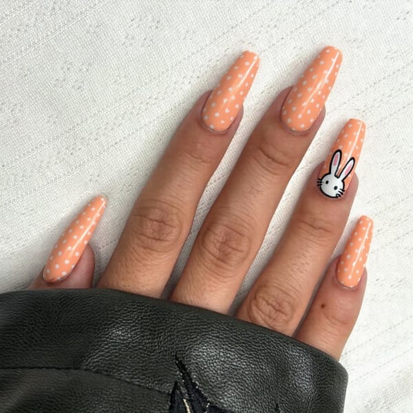 Long stiletto nails in pastel orange with little polka dots and a cute bunny decal on one accent nail.