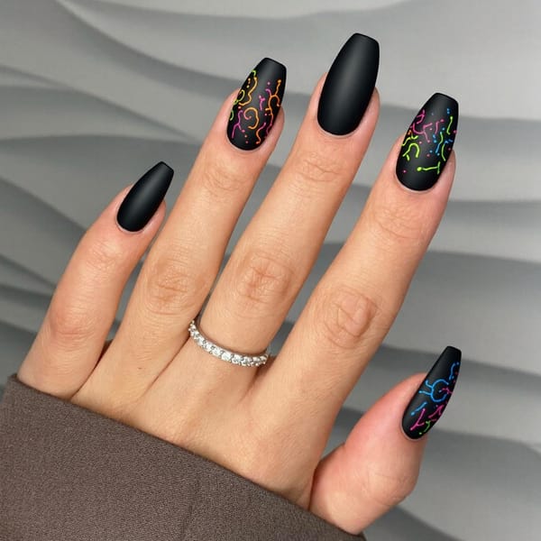 Long almond nails in a matte black base with neon splatter nail art for a cool, artsy finish.