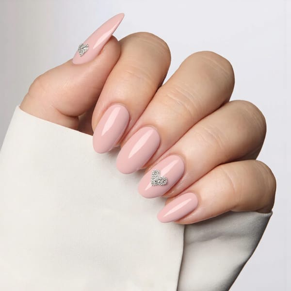 Medium almond nails in a blush pink ombre, each ring finger adorned with a small rhinestone heart for a romantic touch.