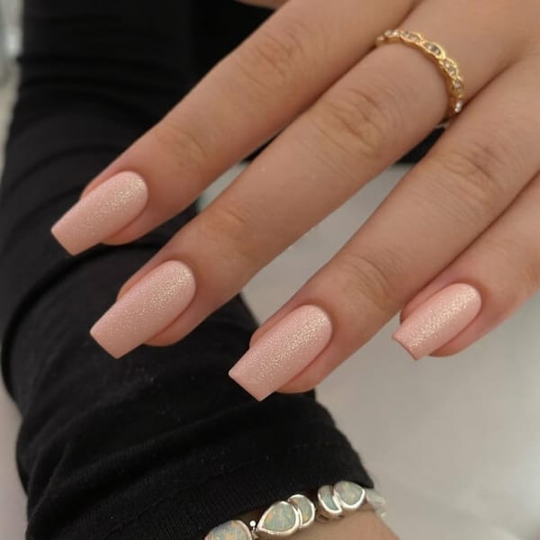 Short stiletto nails in a soft peach with a touch of glitter, ideal for a relaxed vacation style.