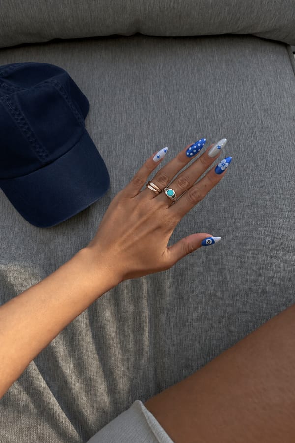 different nails, blue, white, maybe a touch of silver, stars, 8 balls, polka dots, blooming gell Nail shape: stiletto. Nail length: medium. Only change the nails visible in the image to match this design. Keep the rest of the image — the hand, skin, background, lighting, and everything else — exactly the same.