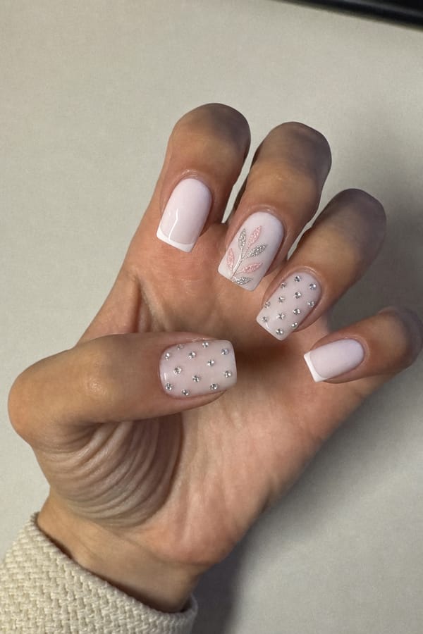milky white base. some with a crisp white French tip. then draw some silver and pink leafs on the ones without the French tip. On others without the French tip add tiny rhinestones all over the nails. Nail shape: square. Nail length: medium. Only change the nails visible in the image to match this design. Keep the rest of the image — the hand, skin, background, lighting, and everything else — exactly the same.