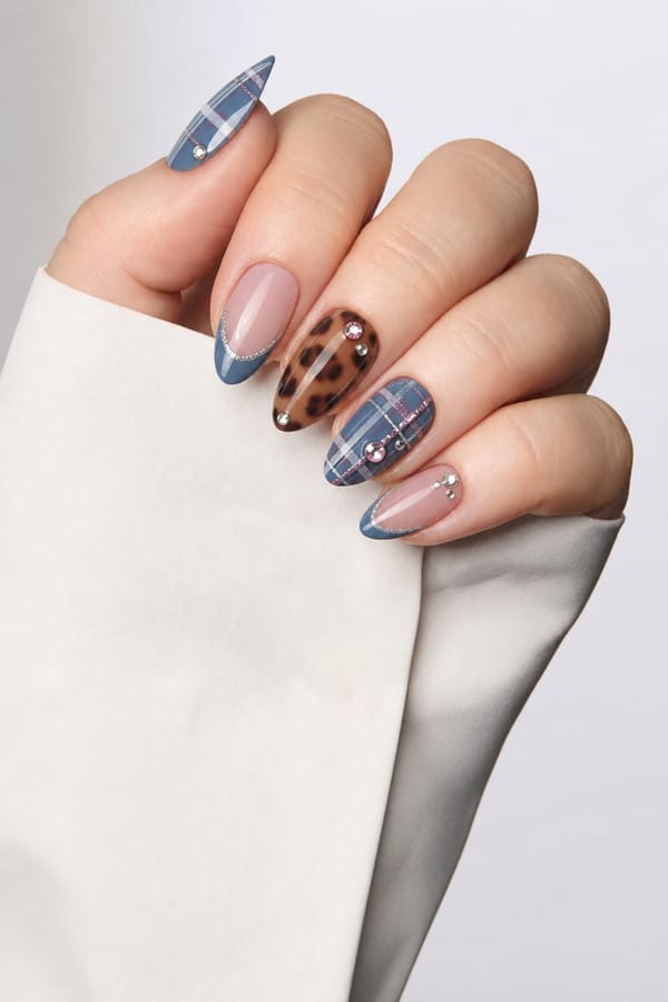 blues and silvers, some plain French tips, brown tortuous print, gems, plaid look, cozy but minimalist for fall add some pink and more gems as well Nail shape: almond. Nail length: medium. Only change the nails visible in the image to match this design. Keep the rest of the image — the hand, skin, background, lighting, and everything else — exactly the same.