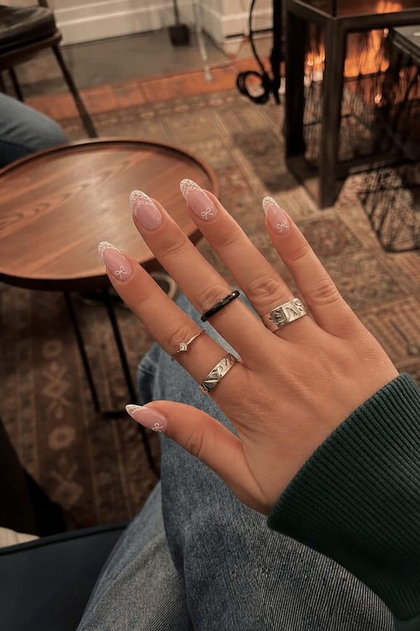 light pink base nails with a white lace French tip and some bows Nail shape: almond. Nail length: short. Only change the nails visible in the image to match this design. Keep the rest of the image — the hand, skin, background, lighting, and everything else — exactly the same.