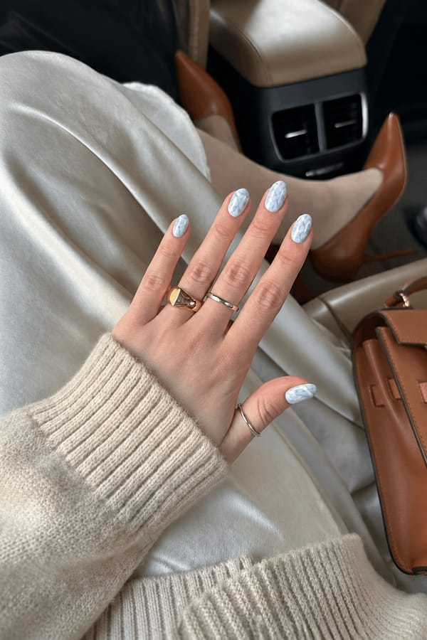 on all of the nails, do a white and light baby blue marble design Nail shape: almond. Nail length: medium. Only change the nails visible in the image to match this design. Keep the rest of the image — the hand, skin, background, lighting, and everything else — exactly the same.