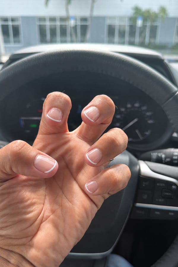 Repair and tidy the fingernails in the image: mend chips, cracks and broken tips, smooth ragged edges, clean up the cuticles, and even out the existing polish where it is worn or smudged. Then style the nails as requested: Base nude transparente con acabado brillante y micro-puntas francesas blancas nítidas, un poco más finas que la francesa clásica. Líneas limpias y contemporáneas.. Apply the styling to the nails only. Beyond the repairs and the requested styling, keep every nail's current shape and length. Keep the rest of the image — the hand, skin, background, lighting, and everything else — exactly the same.