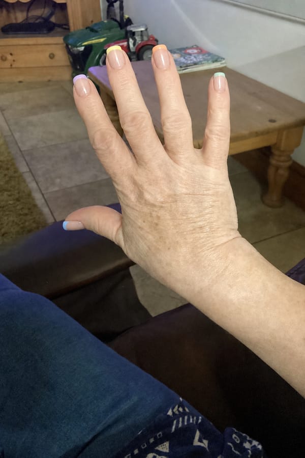 Glossy sheer nude base with pastel French tips. 5 accent nails: each nail features a different soft pastel tip color (lavender, yellow, peach, pink, mint, baby blue tones). Tips are clean and minimal with no outlines or decorations. All nails share the same style, only color varies per nail. Nail shape: square. Nail length: medium. Only change the nails visible in the image to match this design. Keep the rest of the image — the hand, skin, background, lighting, and everything else — exactly the same.