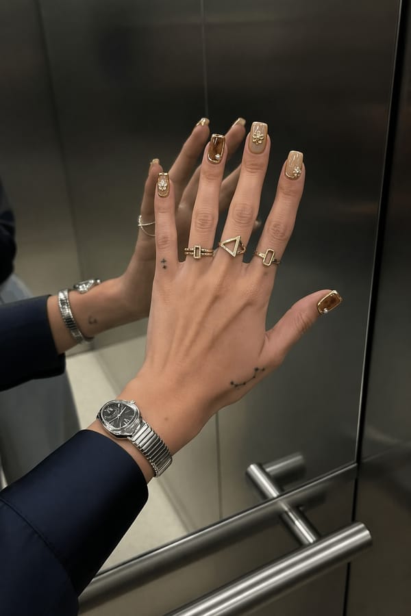 Warm yellow and brown tones with glossy nude accents, gold chrome details, 3D metallic frames, pearl-like elements, and floral embellishments. Luxurious, elegant, high-shine, jewelry-inspired design. Nail shape: square. Nail length: short. Only change the nails visible in the image to match this design. Keep the rest of the image — the hand, skin, background, lighting, and everything else — exactly the same.