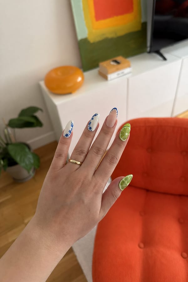 Mixed glossy set, 5 accent nails: 1–2) White base with blue floral/leaf patterns along the edges. 3) Nude base with a blue curved French outline and white dots. 4–5) 3D lime slice designs with translucent green segments and raised texture, placed across the nail surface. Nail shape: almond. Nail length: long. Only change the nails visible in the image to match this design. Keep the rest of the image — the hand, skin, background, lighting, and everything else — exactly the same.