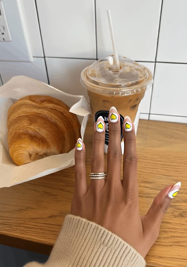 Nails featuring a soft pastel pink base color with a subtle glossy finish. The tips of the nails are adorned with a delicate French manicure in a complementary pastel yellow. On the index and ring fingers, minimal hand-painted lemon slices in pastel pink and yellow add a refreshing summer touch, with each slice featuring just a hint of detail to maintain an elegant and feminine aesthetic. The remaining nails showcase only the pink base, creating a harmonious balance between playful art and simplicity, perfectly suited for medium almond-shaped nails.