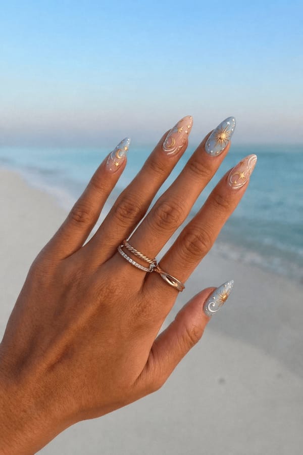 Almond nails, mix of nude and pastel blue bases, celestial theme with gold sun, star, and swirl designs, soft white accents, minimal negative space. Elegant, dreamy aesthetic, glossy finish, close-up hand. Nail shape: almond. Nail length: long. Only change the nails visible in the image to match this design. Keep the rest of the image — the hand, skin, background, lighting, and everything else — exactly the same.