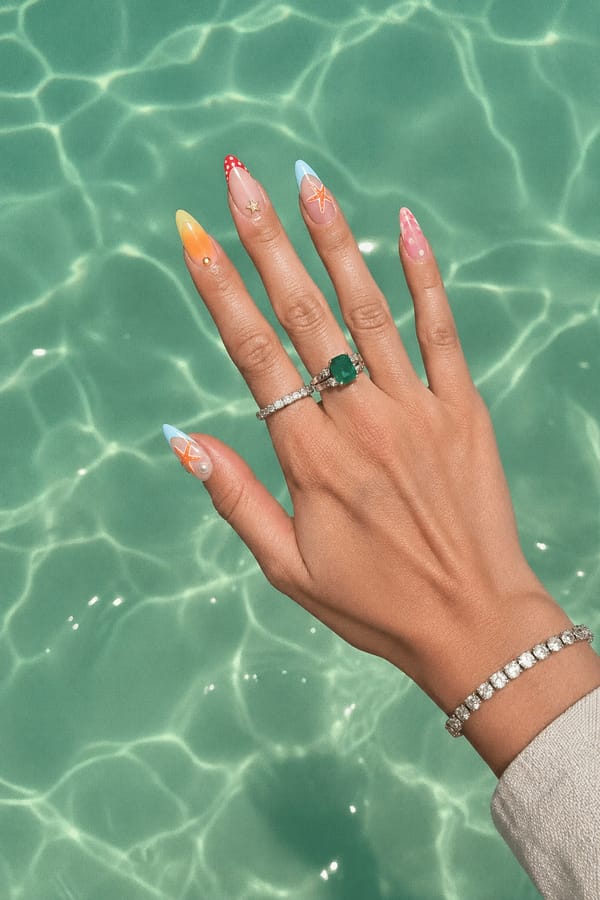 Glossy sheer nude base with mixed summer designs, 5 accent nails: Yellow-orange aura gradient with small gold stud. Nude base with red polka-dot French tip and tiny gold star. Nude base with pastel blue tip and hand-painted starfish. Nude base with pink aura tip and abstract dots. Nude base with pastel blue/orange tips, starfish art, and small pearl accents. Nail shape: almond. Nail length: long. Only change the nails visible in the image to match this design. Keep the rest of the image — the hand, skin, background, lighting, and everything else — exactly the same.