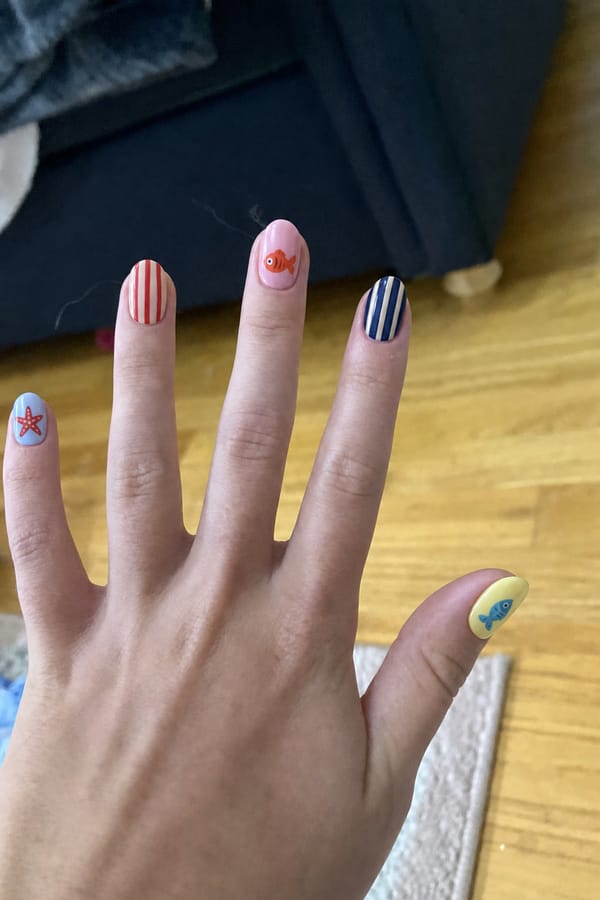 Mixed glossy set, 5 accent nails: Pastel blue base with hand-painted starfish. Nude base with red vertical stripes. Soft pink base with small orange fish illustration. Navy base with beige vertical stripes. Pale yellow base with blue fish illustration. Nail shape: almond. Nail length: short. Only change the nails visible in the image to match this design. Keep the rest of the image — the hand, skin, background, lighting, and everything else — exactly the same.