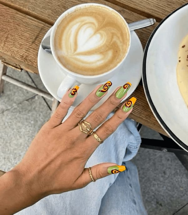 Nails designed with a nostalgic 70s aesthetic, featuring a base color of soft avocado green across all nails for a cohesive look. On the ring fingers, delicate swirls in burnt orange and mustard yellow create a playful yet elegant design that captures the essence of retro style. The swirls are minimal, with no more than four lines gracefully winding across each nail to maintain a chic simplicity. The finish is glossy to enhance the vibrant colors and give a polished look, perfectly complementing the medium almond shape of the nails.