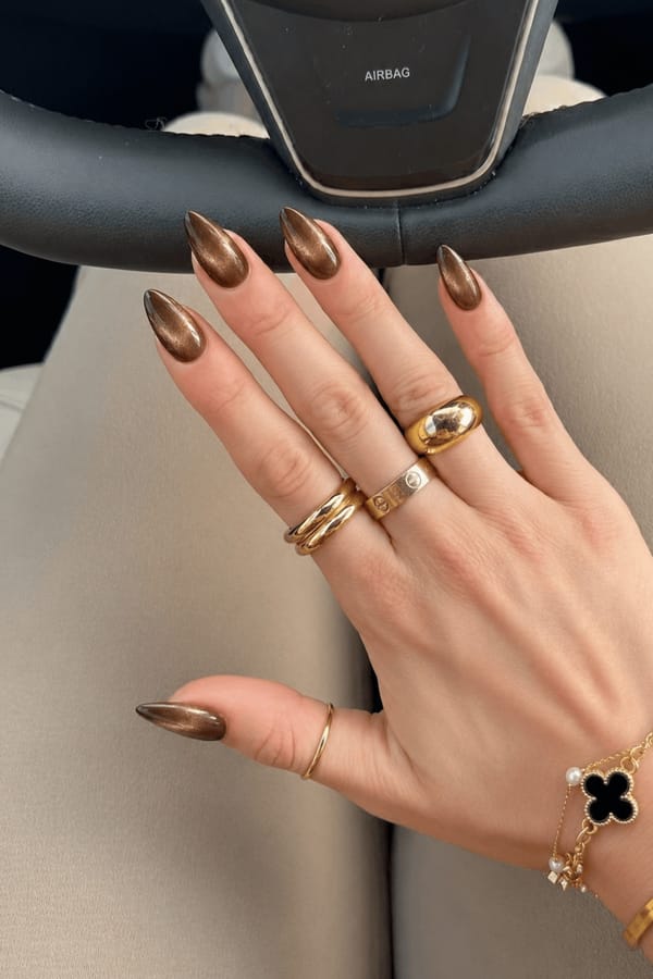 Uniform glossy metallic design with no accent nails (0 accent fingers). All nails feature a deep brown to bronze cat-eye effect with a soft magnetic shimmer concentrated through the center, creating a dimensional reflective stripe. Smooth gradient edges with a glassy finish, no अतिरिक्त patterns or decorations. Nail shape: stiletto. Nail length: medium. Only change the nails visible in the image to match this design. Keep the rest of the image — the hand, skin, background, lighting, and everything else — exactly the same.
