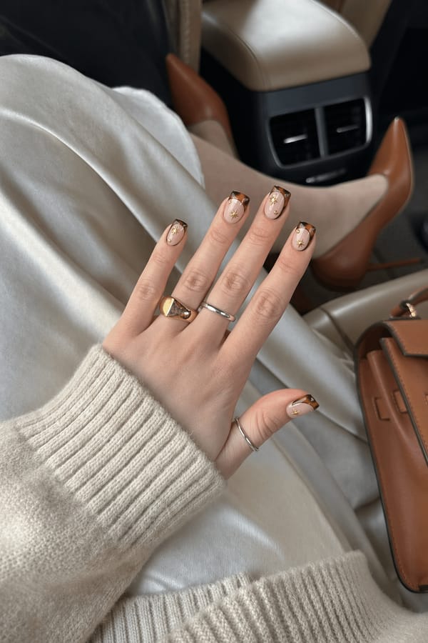 Sheer nude base with glossy tortoiseshell accents, dark brown outlines, gold starburst details, and small gold bead embellishments. Elegant, warm-toned, luxe aesthetic. Nail shape: square. Nail length: medium. Only change the nails visible in the image to match this design. Keep the rest of the image — the hand, skin, background, lighting, and everything else — exactly the same.