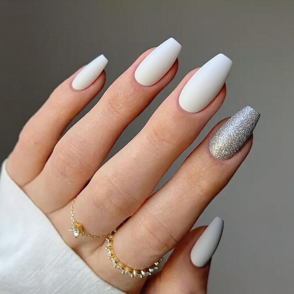 Medium stiletto nails in matte white with one accent nail covered in chunky silver glitter.