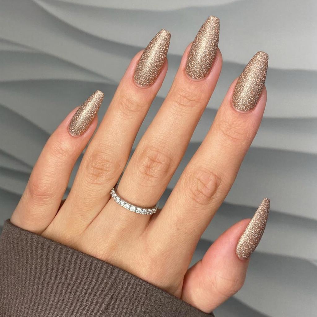 Long almond nails in a glittery champagne shade with subtle festive patterns for an elegant holiday style.