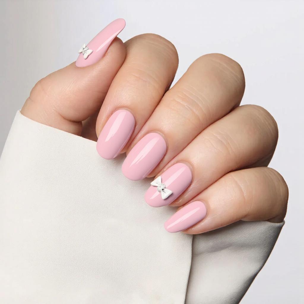Medium almond nails in a bubblegum pink, each with a tiny white bow on the ring finger for a cute twist.