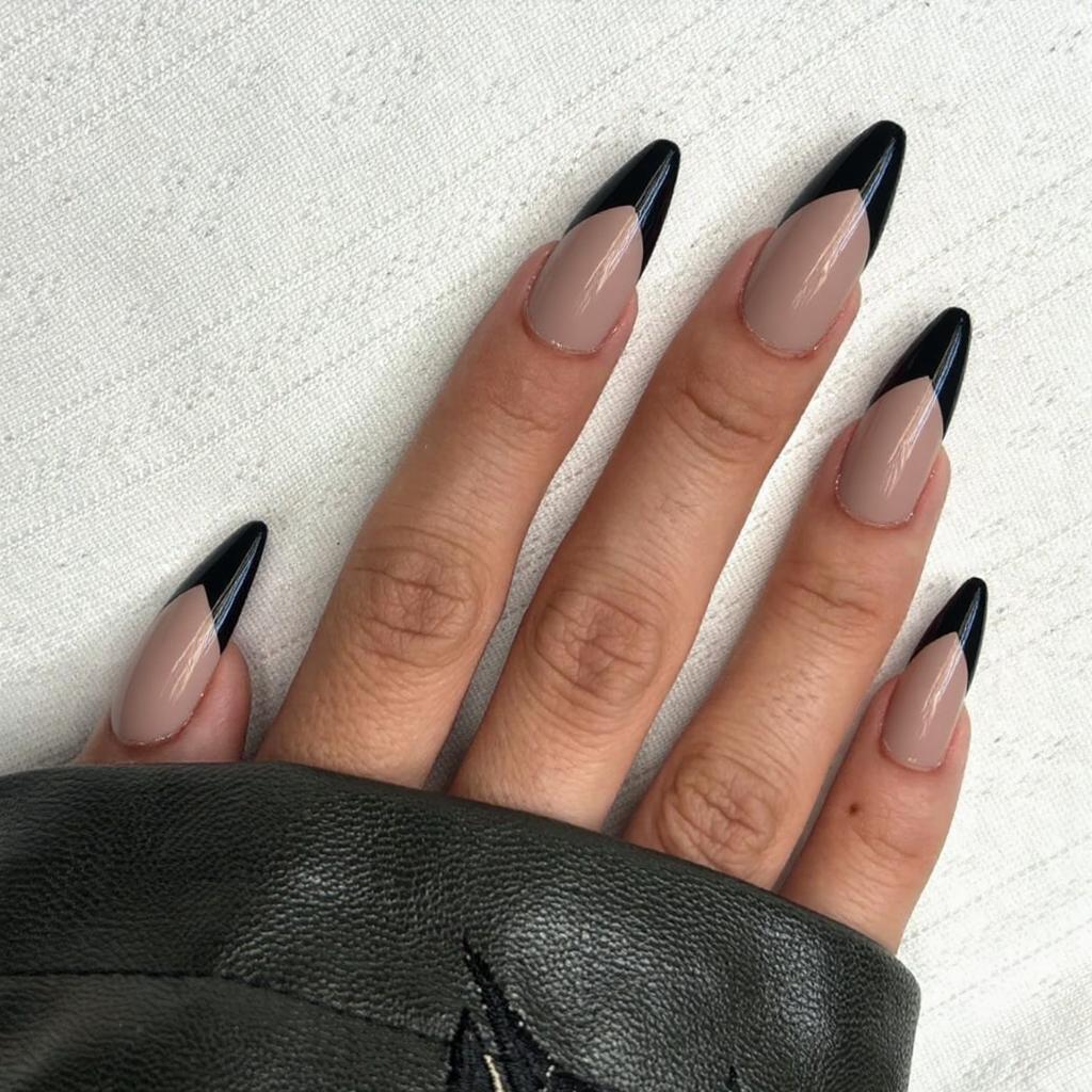 Long stiletto nails with a dramatic French tip in black, contrasting against a sheer nude base.