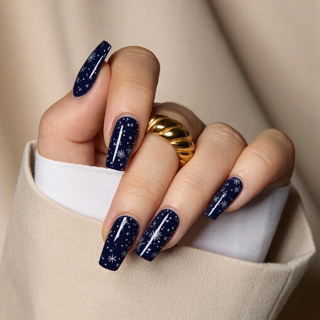 Medium square nails in a deep navy blue, each adorned with tiny snowflake designs for a wintery vibe.