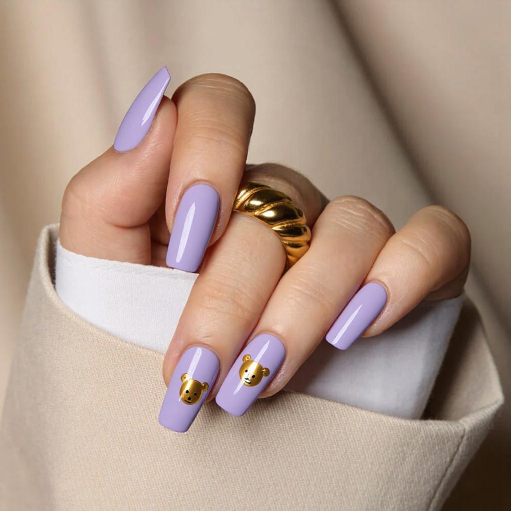 Medium square nails in pastel purple with a small teddy bear face on each ring finger.