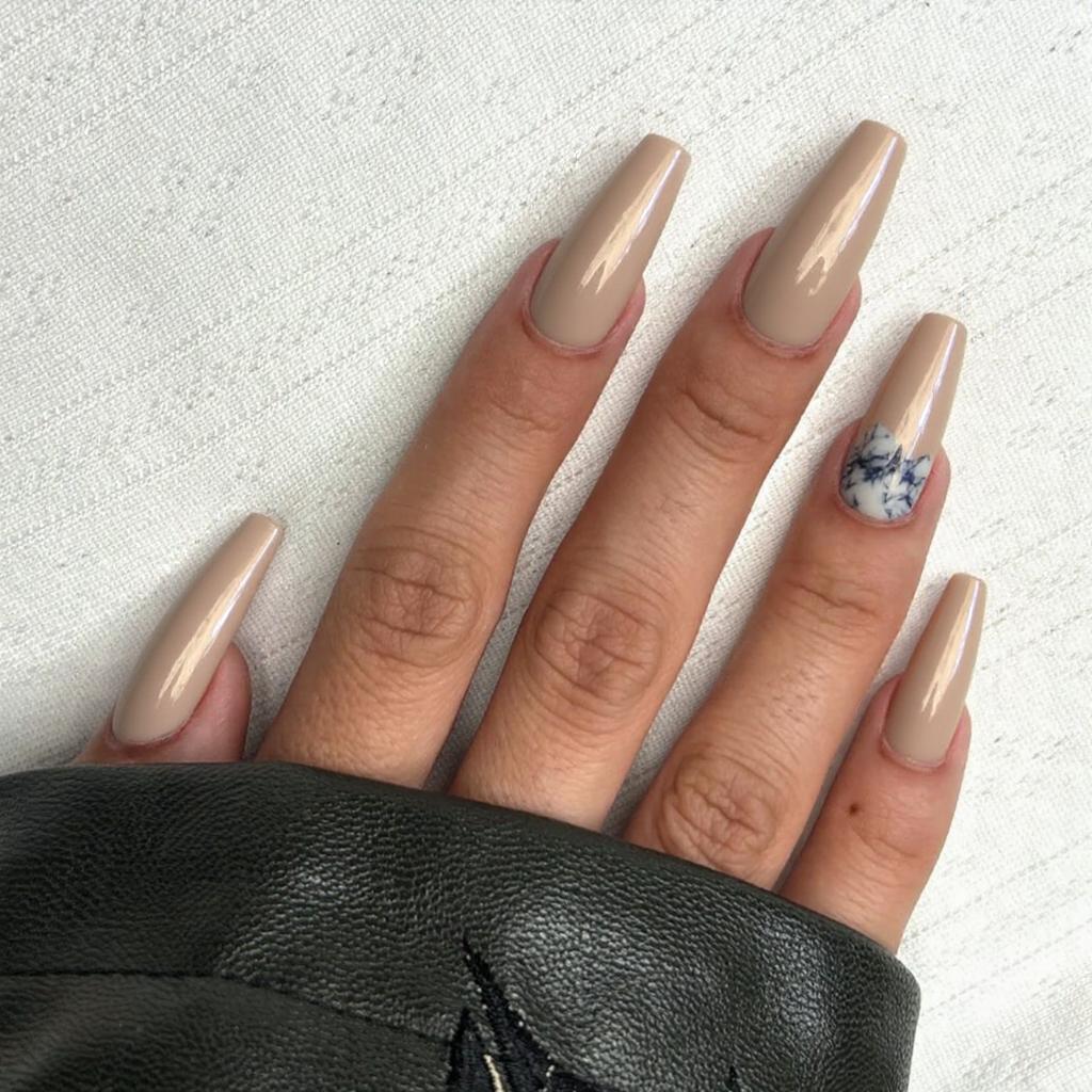 Long stiletto nails in an elegant champagne shade, each ring finger boasting a delicate marble accent for a special occasion.