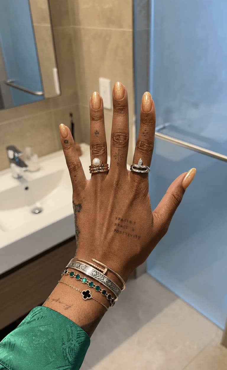 Warm honey-gold shimmer, short almond nails, glossy finish, featuring a soft ombre fade from amber to champagne on every nail. Nail shape: almond. Nail length: short. Only change the nails visible in the image to match this design. Keep the rest of the image — the hand, skin, background, lighting, and everything else — exactly the same.