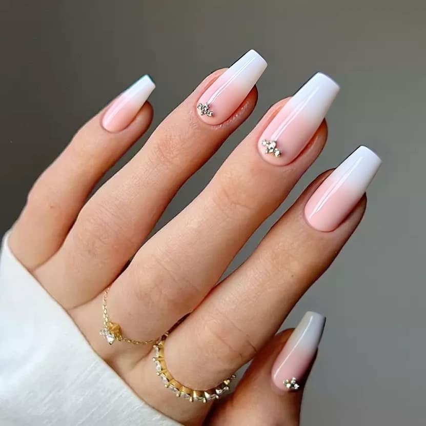 Nails painted in a soft pastel pink base that exudes elegance, with a glossy finish enhancing the delicate hue. On the middle fingers, minimalist designs feature a subtle gradient shifting into a gentle blush, adorned with a few small, sparkling rhinestones clustered near the cuticle, creating a sophisticated look. The other nails are left in a pristine pastel pink to maintain a harmonious balance, perfect for medium stiletto nails.