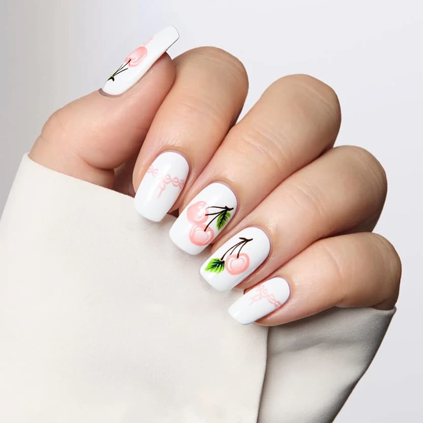 Nails featuring a classic white French tip that delicately curves along the edges, enhancing the elegant almond shape. On the ring fingers, a charming design of soft pastel cherry illustrations, artfully arranged with minimal detail to maintain a sophisticated look. Dainty lace accents in a subtle pale pink are delicately placed along the cuticle line of the same nails, adding a touch of femininity. The remaining nails keep a pristine white base, providing balance and allowing the accent nails to pop. A glossy finish completes the look, giving the nails a polished and refined appearance.