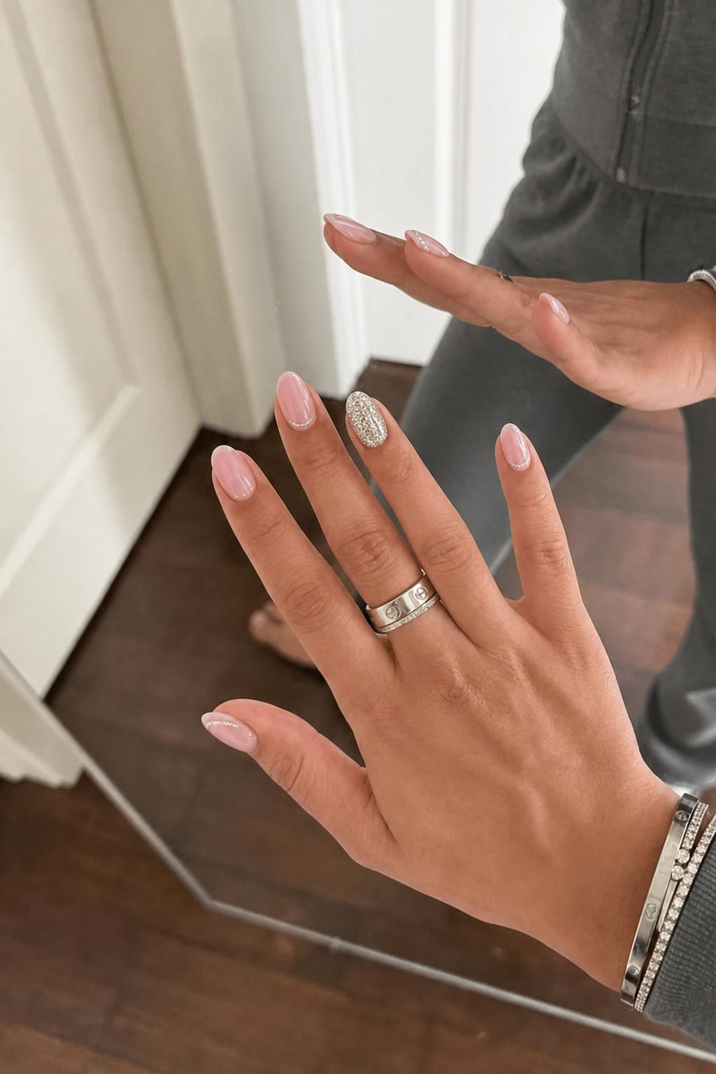 Glossy sheer pink base on every nail. One accent nail fully covered in fine holographic silver glitter. Two nails with a thin glitter stripe near the tip. Nail shape: almond. Nail length: short. Only change the nails visible in the image to match this design. Keep the rest of the image — the hand, skin, background, lighting, and everything else — exactly the same.