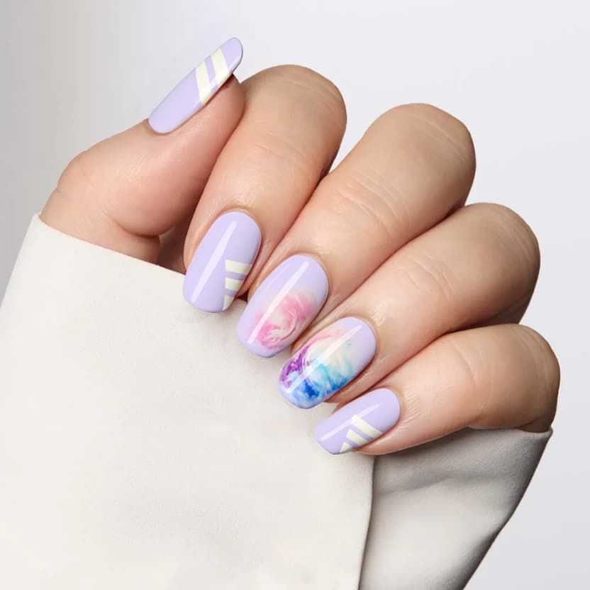 Elegant almond-shaped nails painted in a soft pastel lavender hue, providing a gentle and refined backdrop perfect for a school setting. The pinky and ring fingers feature subtle, minimalistic white stripes running diagonally from the corners, adding a touch of sophistication without being overwhelming. The middle finger showcases a delicate watercolor swirl effect in pastel tones of pink and blue, capturing a serene, artistic aesthetic. The index and thumb nails remain unadorned, maintaining the simplicity and elegance of the overall design. A glossy finish enhances the pastel colors, making this design both practical and stylish for everyday school wear.