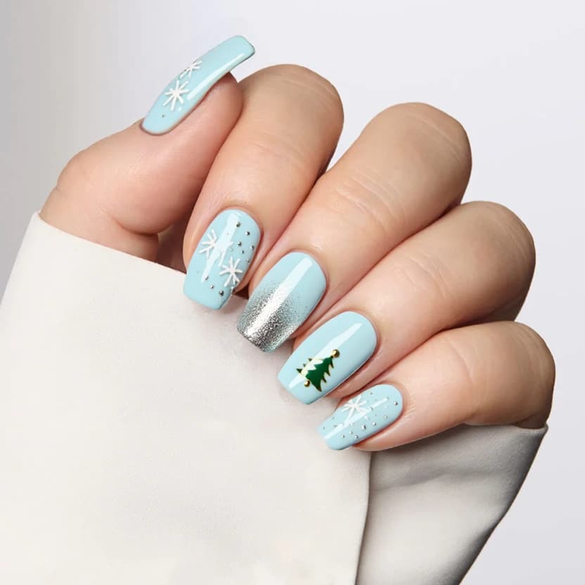 Elegant almond-shaped nails featuring a soft pastel blue base color that evokes a wintry sky. On the index and ring fingers, delicate white snowflakes are hand-painted, subtly accentuated by tiny silver glitter dots that mimic falling snow. The middle finger showcases a minimalist Christmas tree in muted green with tiny gold embellishments representing ornaments, keeping the design simple yet festive. A faint silver bubble effect flows across the remaining nails, adding a whimsical touch to this snowy scene. A glossy finish enhances the overall look, making it perfect for the cozy holiday season while maintaining an elegant and feminine vibe.