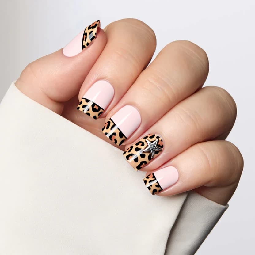 Nails featuring a soft pastel pink base color, creating a delicate and feminine look. The tips of the nails are adorned with a subtle cheetah print design, incorporating soft, muted browns and tans to maintain an elegant vibe. On the ring fingers, a charming star charm is attached, adding a touch of whimsical flair. The other nails display a refined airbrushed effect in pink alongside the cheetah print French tips, enhancing the cohesive theme. The design is complemented by a glossy finish, which adds shine and depth, perfectly suited for the short square shape, ensuring a balanced and chic aesthetic.