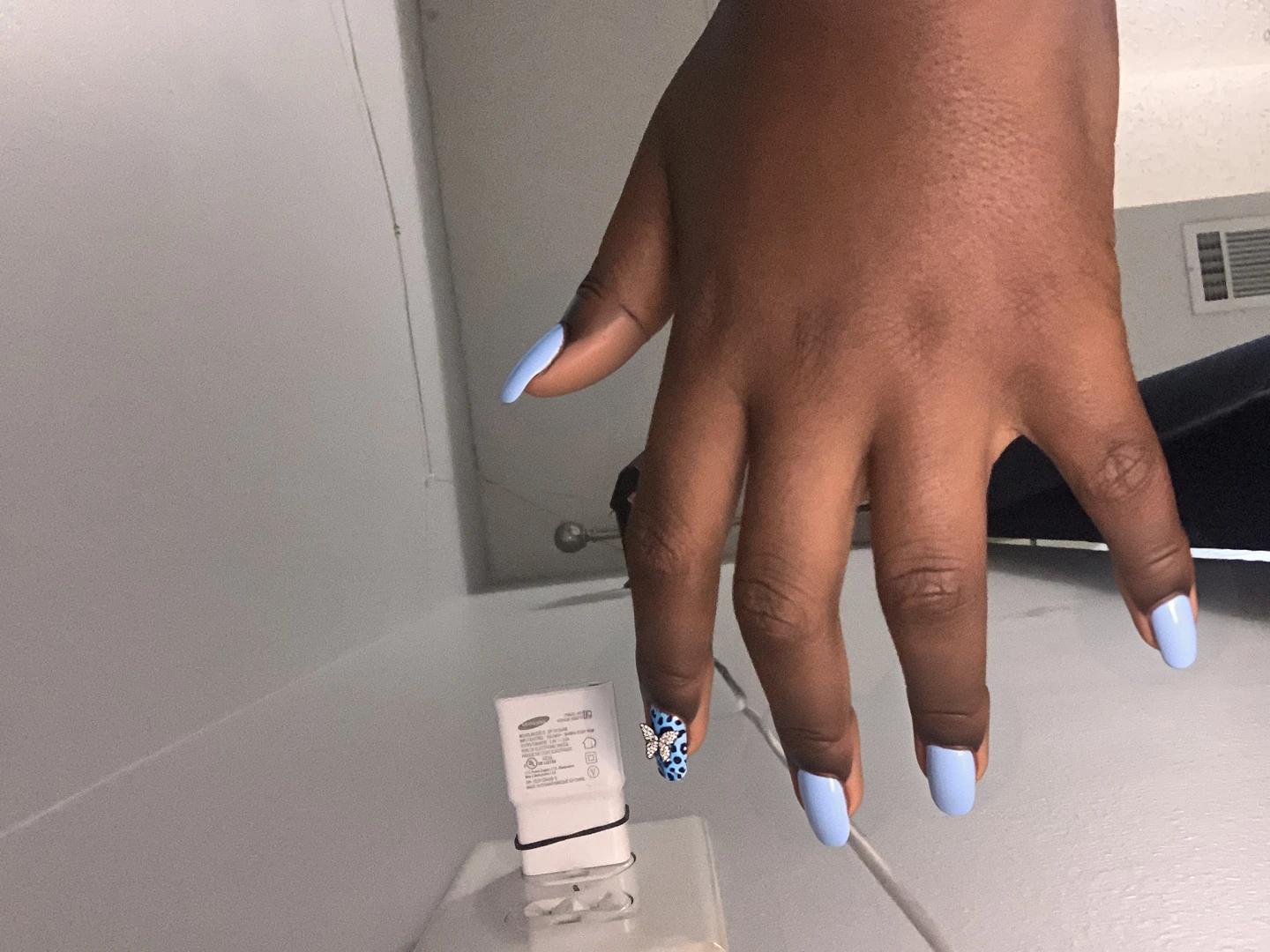 Nails designed with a classic light blue French tip, complemented by a subtle blue cheetah print on the ring finger, adding a playful yet chic element to the overall look. The middle finger features a delicate arrangement of tiny rhinestones, adding a touch of sparkle without overwhelming the minimalist aesthetic. The pinky showcases a charming butterfly charm set against a smooth light blue base, further enhancing the feminine vibe of the design. The remaining nails maintain the elegant light blue base, ensuring a cohesive color scheme that looks polished and trendy, perfectly suited for short square nails.