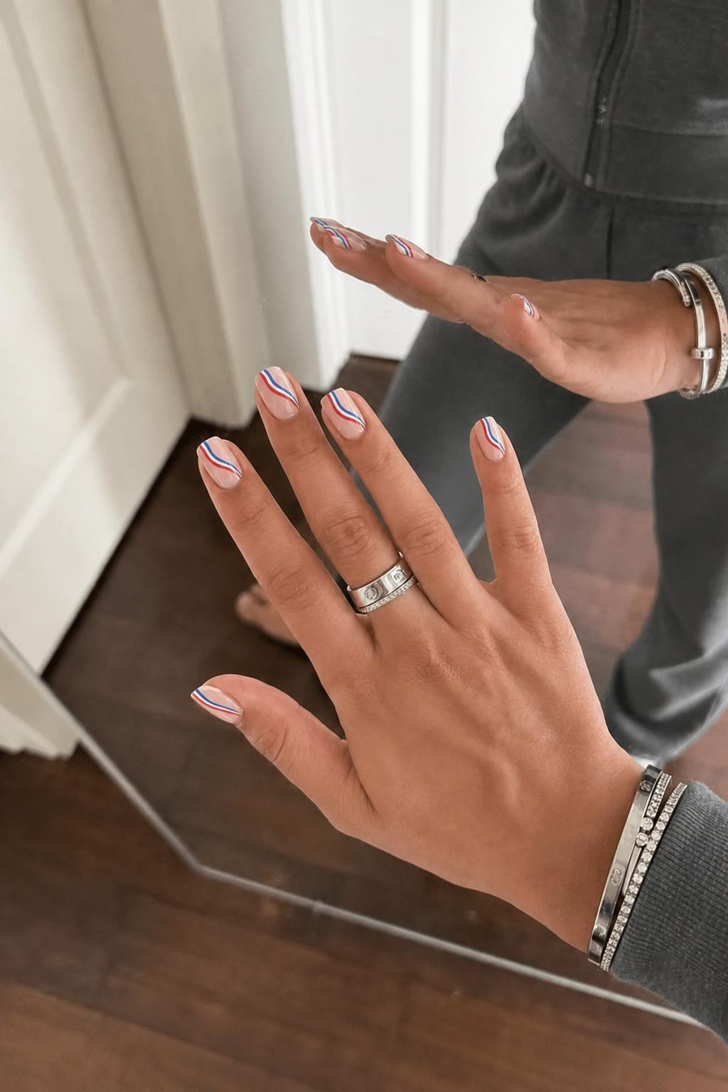 red white and blue swipe lines on nude nails Nail shape: almond. Nail length: short. Only change the nails visible in the image to match this design. Keep the rest of the image — the hand, skin, background, lighting, and everything else — exactly the same.