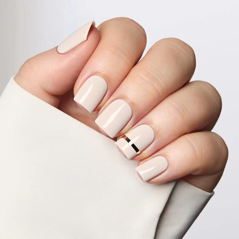 Short square nails elegantly polished in a soft nude beige shade that exudes professionalism and understated elegance. The majority of the nails maintain a smooth, glossy finish, while the ring finger features a single, thin metallic stripe running vertically down the center, providing a touch of shine without overwhelming the minimalist aesthetic. The overall design remains refined and suitable for a corporate setting, striking a balance between simplicity and chic sophistication—perfectly tailored for short square nails.