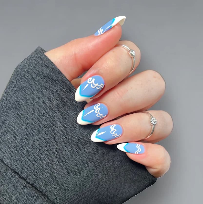 Nails showcased in a sophisticated French manicure style featuring a serene pastel blue base that elegantly captures the essence of the ocean. The tips are adorned with a delicate, shimmering pearlescent white, subtle yet refined, perfectly complementing the almond shape of the nails. To evoke the beach theme, tiny hand-painted white waves gracefully curl along the edges of the ring fingers, enhancing the elegant look without overwhelming the design. The remaining nails maintain the soothing blue tone with a glossy finish, creating a beautiful and harmonious balance that exudes a sense of formal chic.