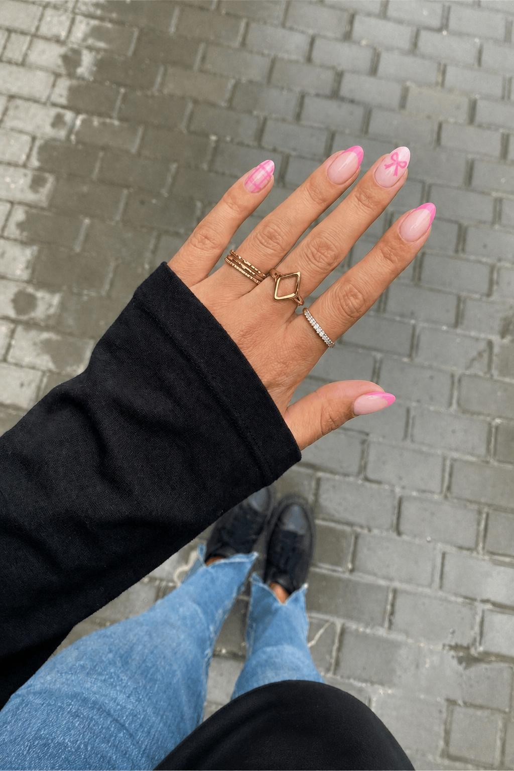 thumb: pink French tip pointer finger: jelly plaid with light and bright pink middle finger: pink French tip left index finger: bright pink bow facing away with light pink background pinky: pink French tip Nail shape: almond. Nail length: medium. Only change the nails visible in the image to match this design. Keep the rest of the image — the hand, skin, background, lighting, and everything else — exactly the same.