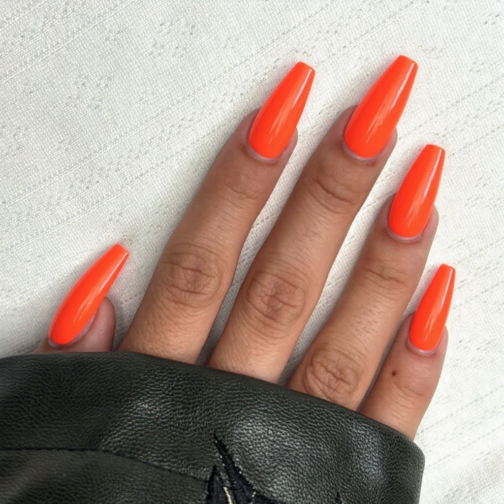 Long stiletto nails in a vibrant neon orange with a high-gloss finish, capturing the energetic trends of 2025.