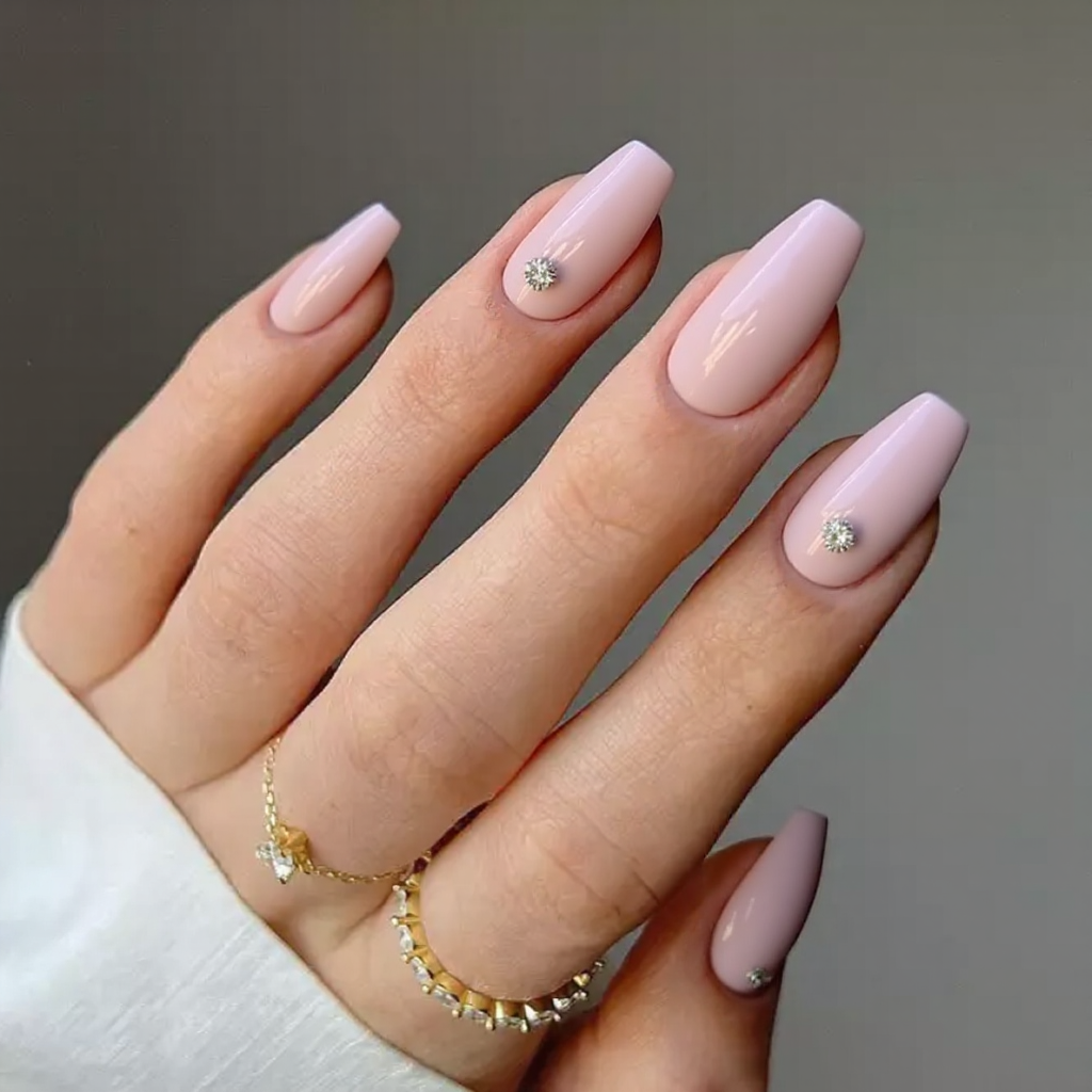 Medium stiletto nails in a pastel pink, each with a tiny rhinestone near the cuticle for subtle sparkle.