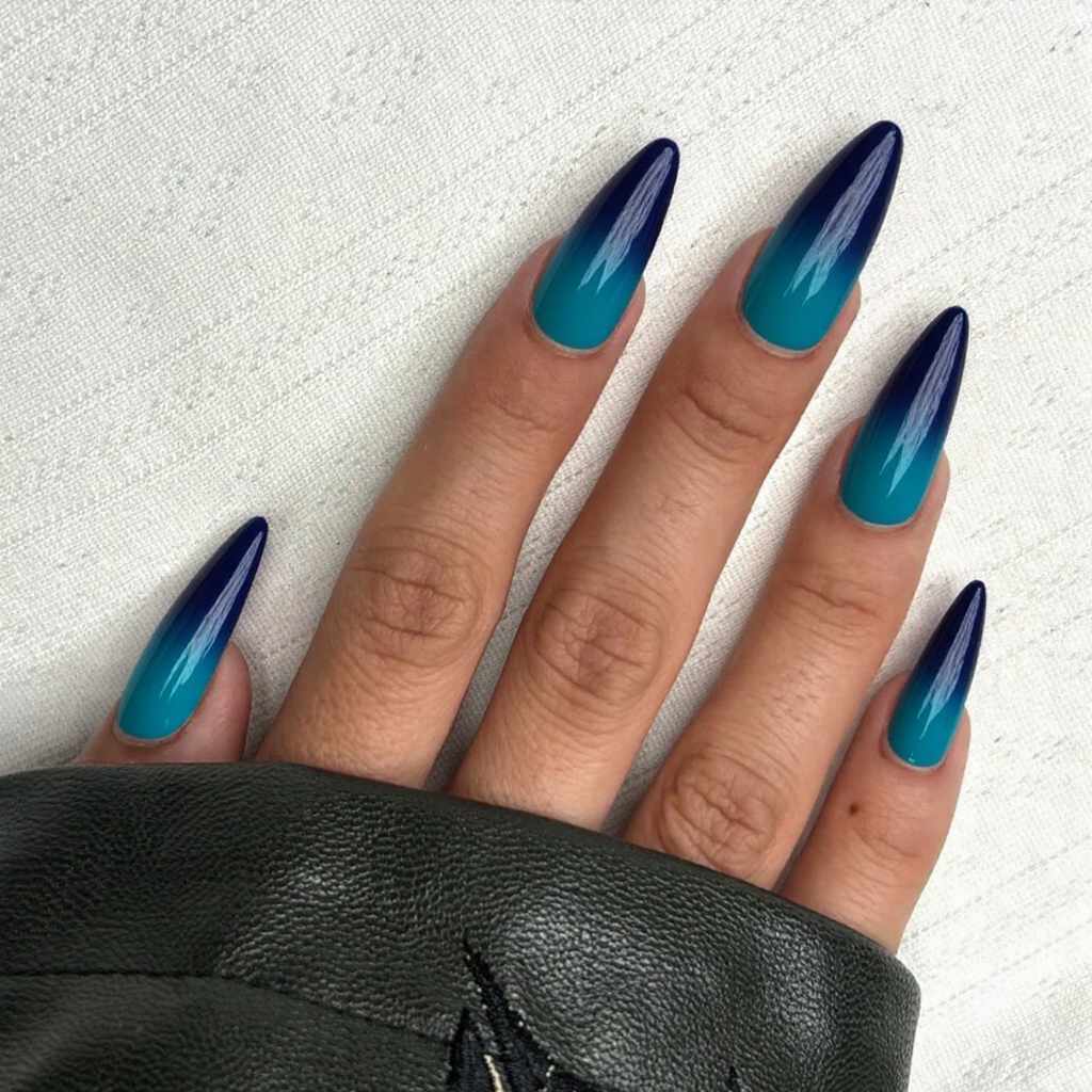Long stiletto nails in a navy ombre fading into a vibrant turquoise at the tips for a dramatic effect.