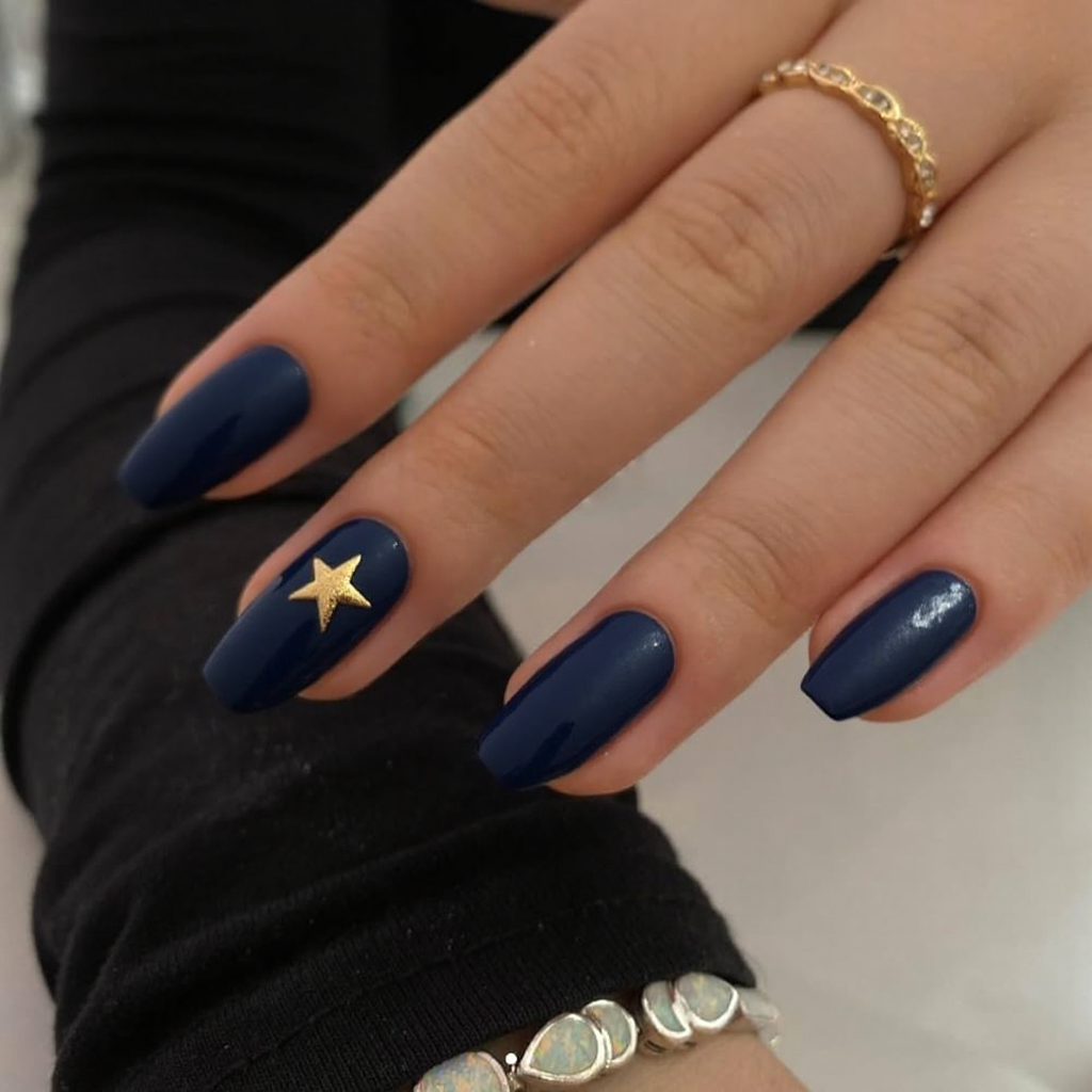 Short stiletto nails in navy blue, with a single gold star on the ring finger for a fun detail.