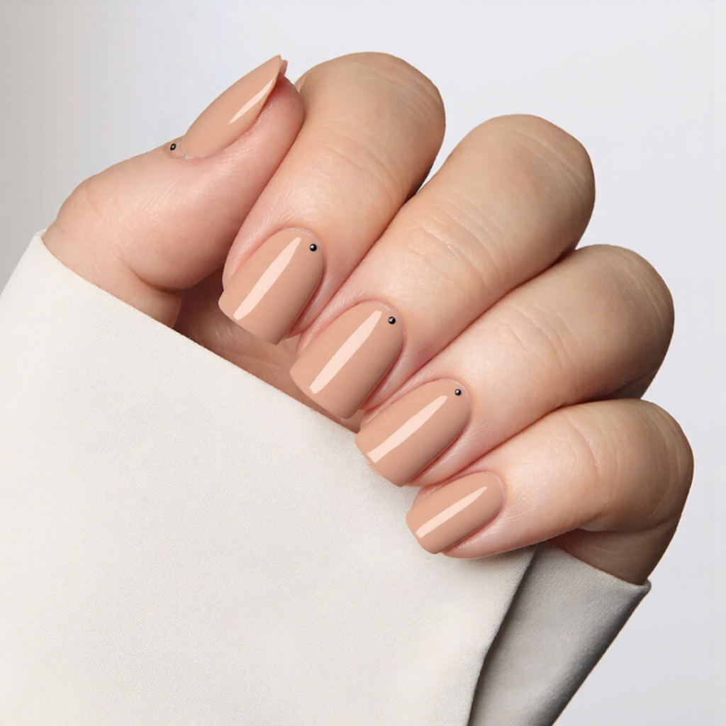 Short square nails in a peachy nude, each with a single black dot near the cuticle for a minimalist vibe.