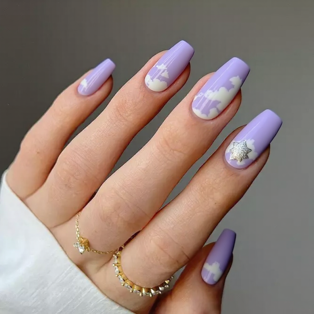 Medium stiletto nails in a lilac base with softly painted clouds and a hint of shimmer on one accent nail.