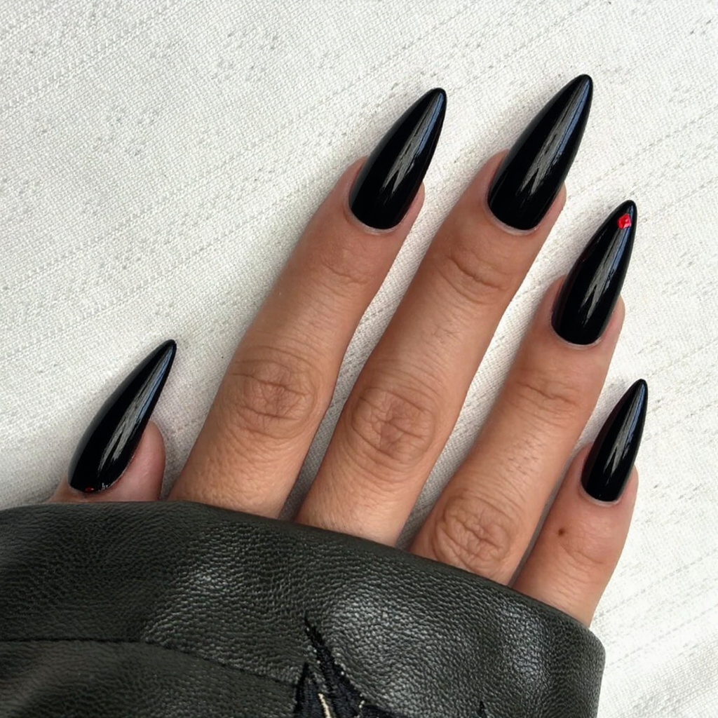 Long stiletto nails in a glossy black, each with a single small red gem at the tip for drama.