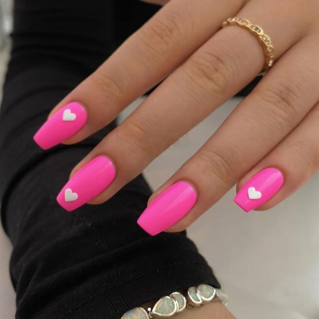 Short stiletto nails in neon pink, each with a tiny white heart near the cuticle for a cute pop.