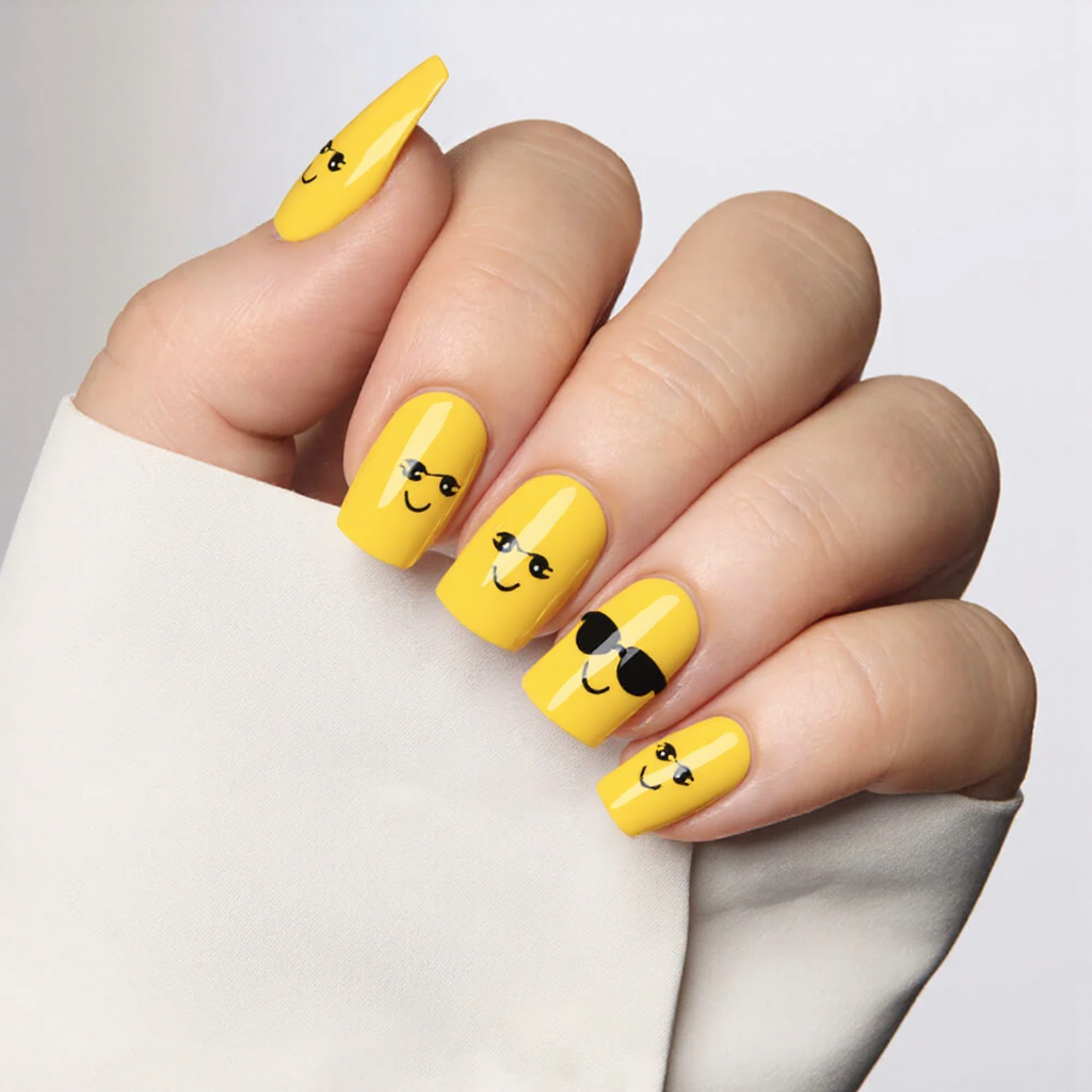 Medium almond nails in a sunny yellow with tiny sunglasses decals for a cheerful summer vacation look.