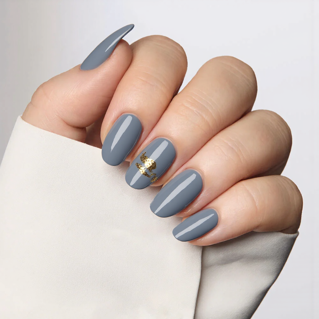 Medium almond nails in a dusty blue hue, adding a small gold foil detail on the middle and ring fingers.