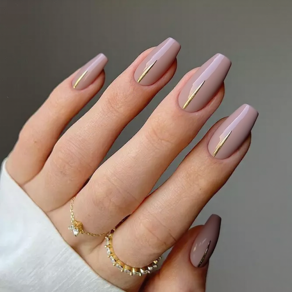 Medium stiletto nails in a dusty pink, accented by a thin gold foil line down the center of each nail.